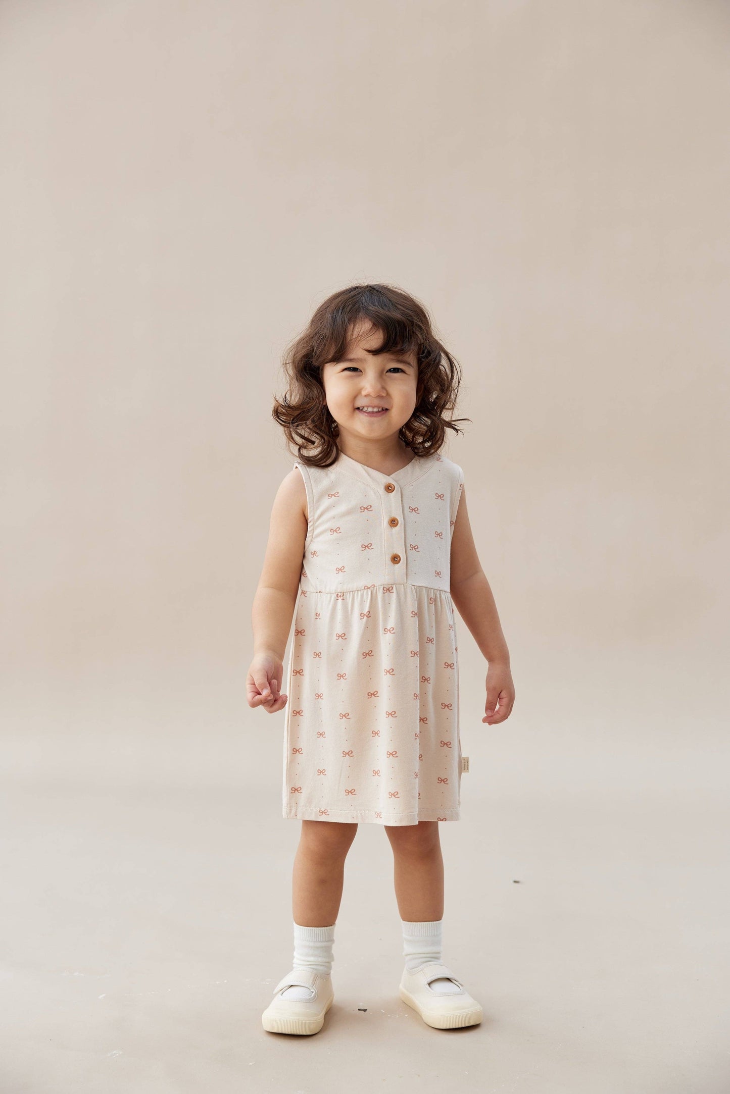 Young child wearing a patterned dress on a plain background.