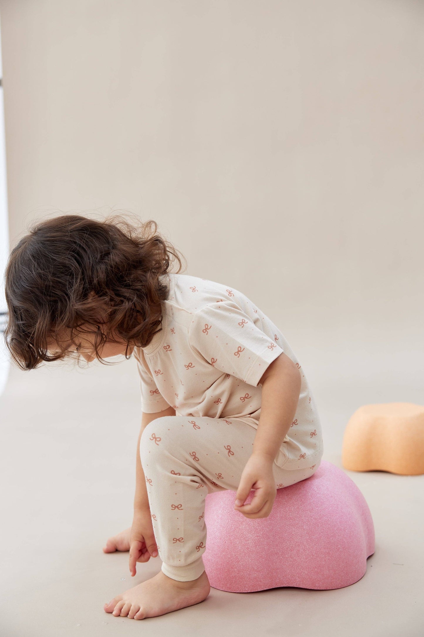 
                  
                    Child sitting on a pink cushion on a plain background.
                  
                