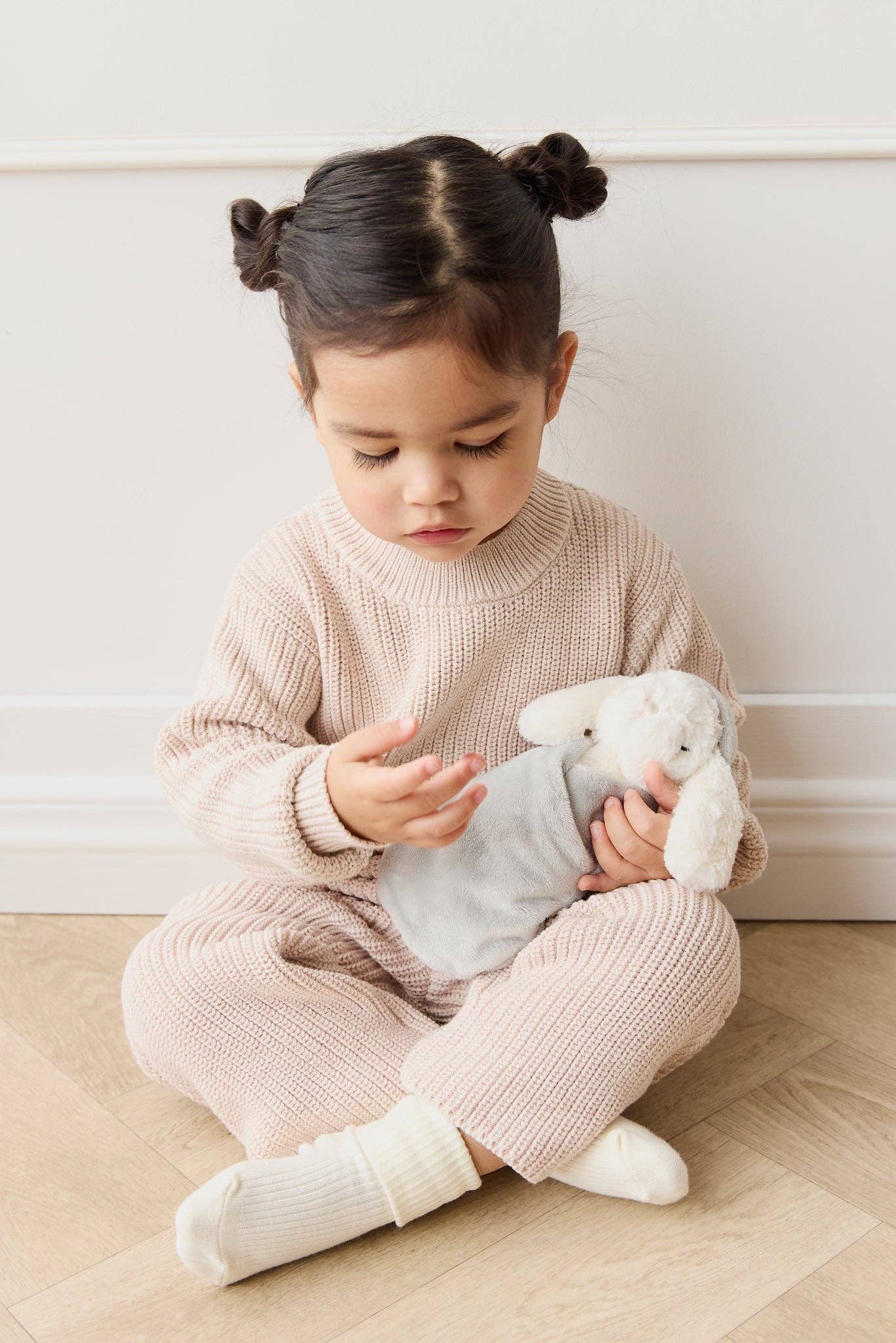 
                  
                    Child sitting on the floor holding a plush bunny against a white wall.
                  
                