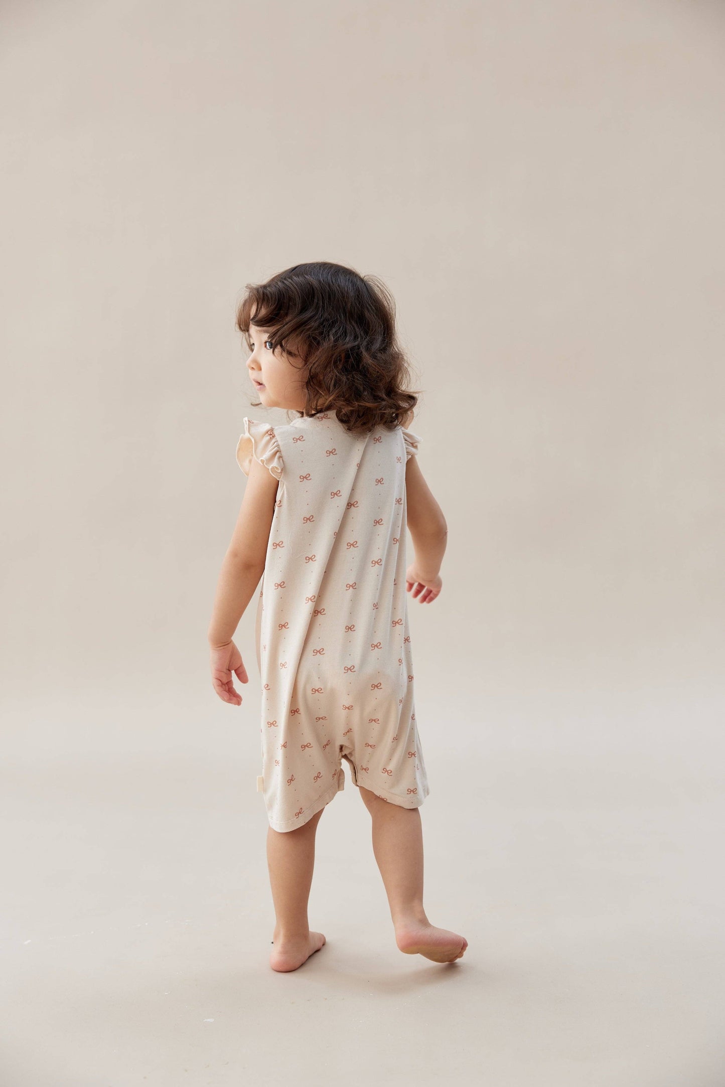 
                  
                    Child wearing a patterned romper on a plain background.
                  
                