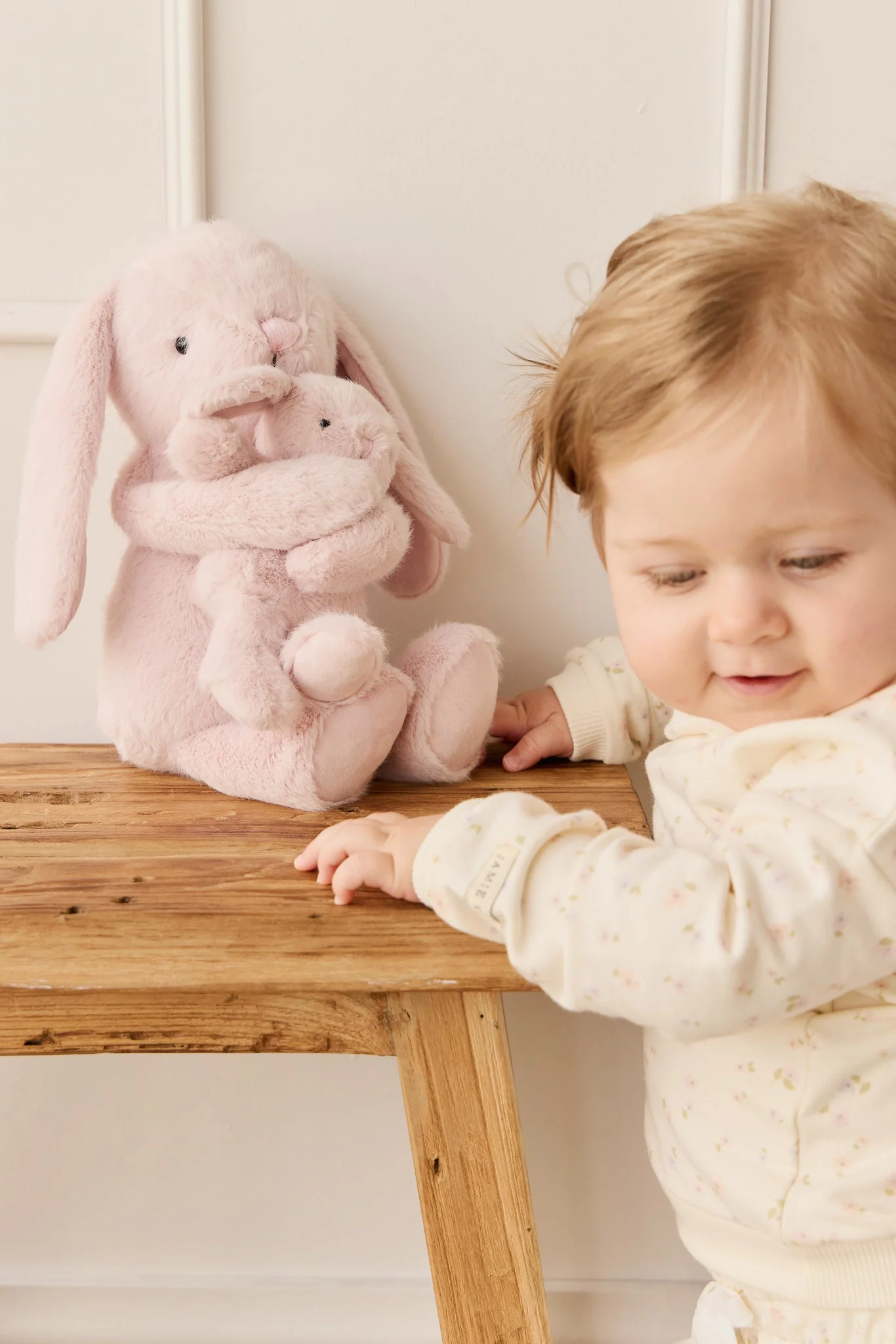 
                  
                    Child interacting with a pink plush bunny toy on a wooden table.
                  
                
