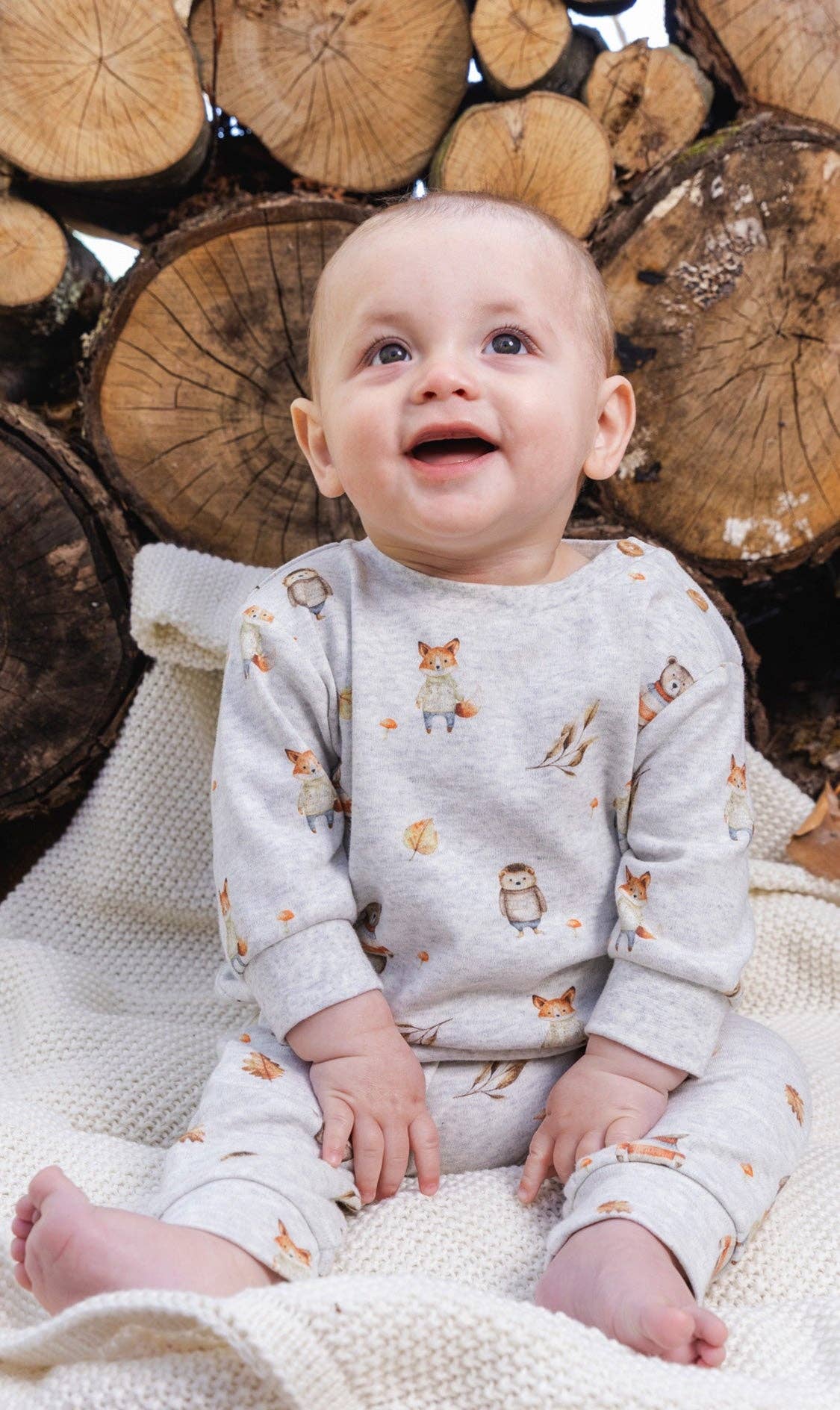 
                  
                    Baby in a patterned outfit sitting on wooden logs.
                  
                