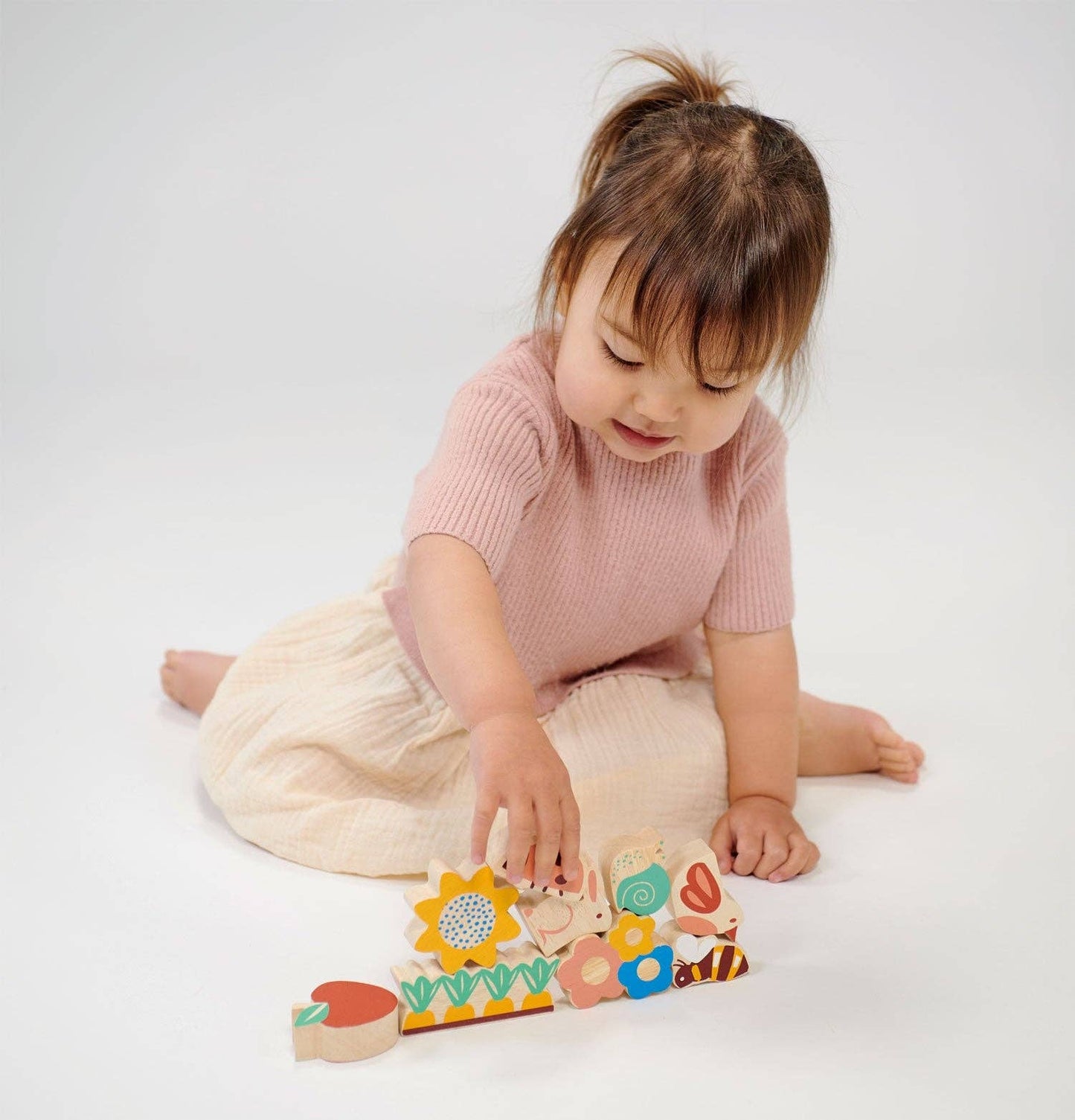 
                  
                    Child playing with a colorful wooden puzzle on a white background.
                  
                