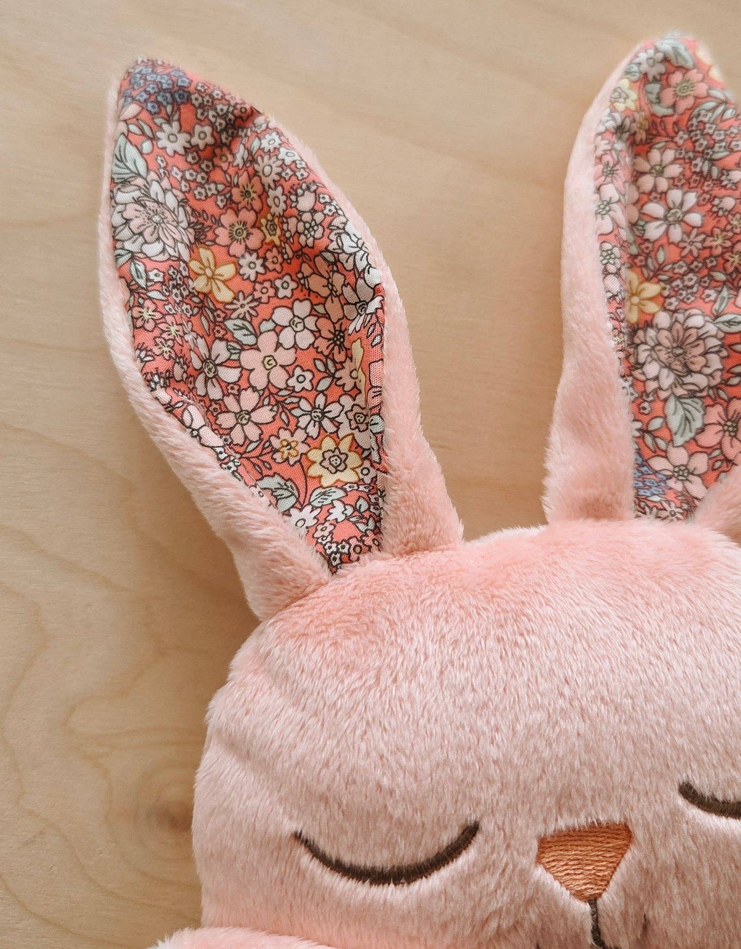 
                  
                    Close-up of a pink plush bunny with floral ears against a wooden background.
                  
                