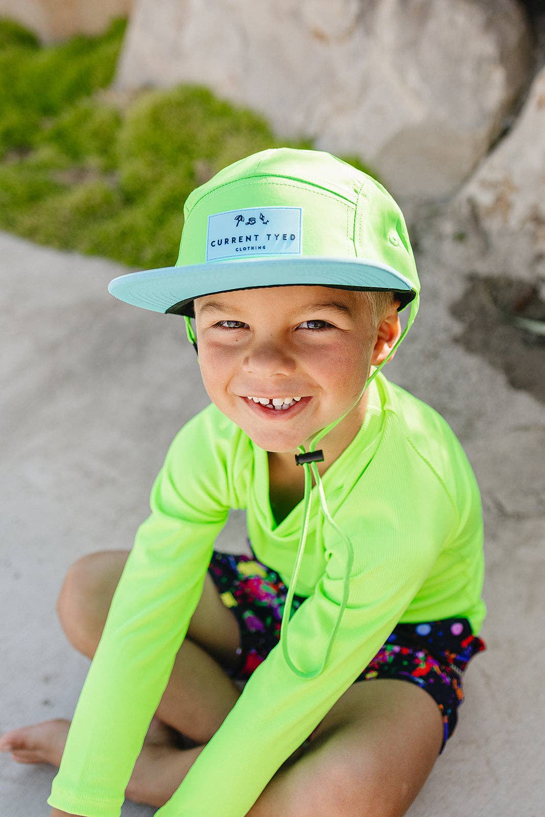 
                  
                    Child wearing a bright green outfit and cap on a beach
                  
                