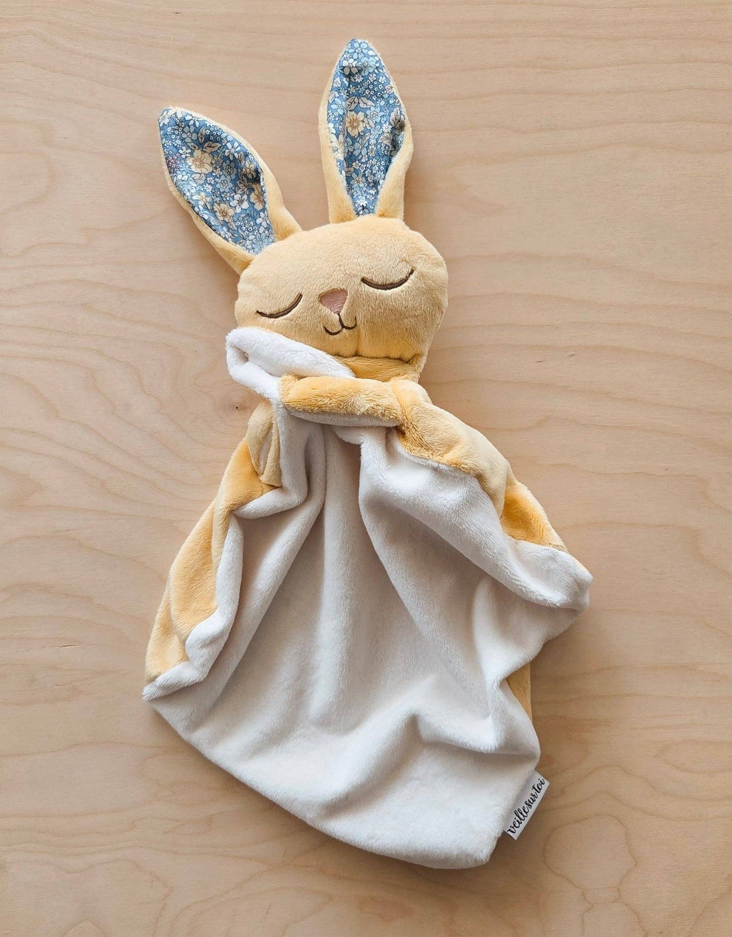 
                  
                    Plush rabbit toy with floral ears on a wooden surface.
                  
                