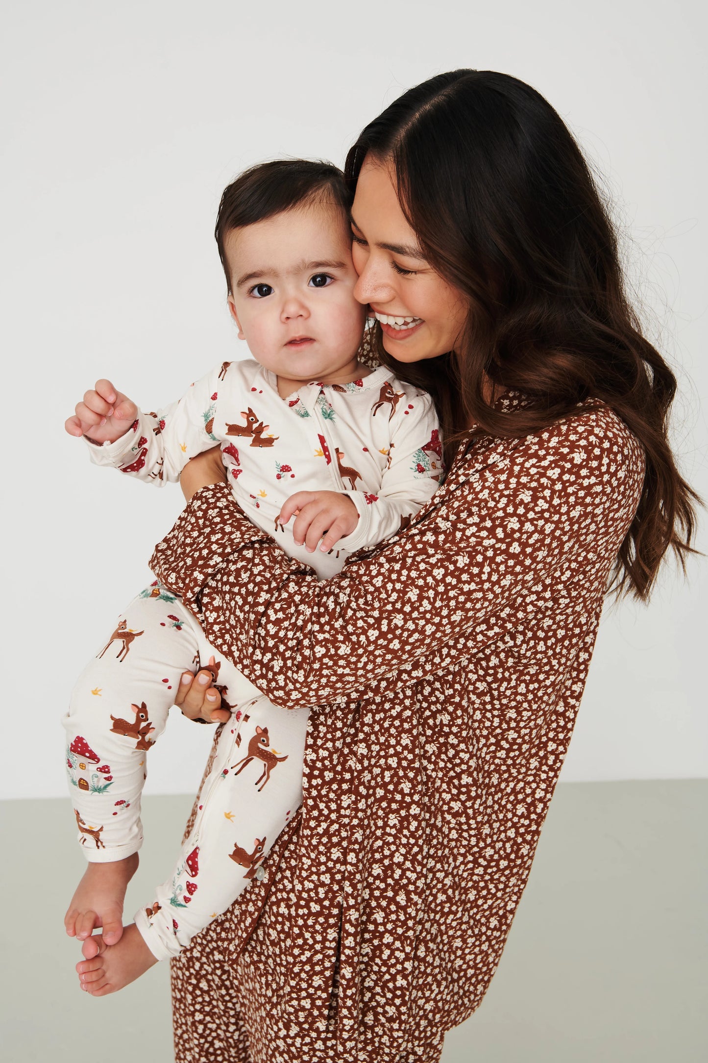 
                  
                    A woman holding a baby wearing matching pajamas. The baby is in an off-white long-sleeve pajama set with a brown deer print, and the woman wears a brown long-sleeve top with a small white floral pattern.
                  
                