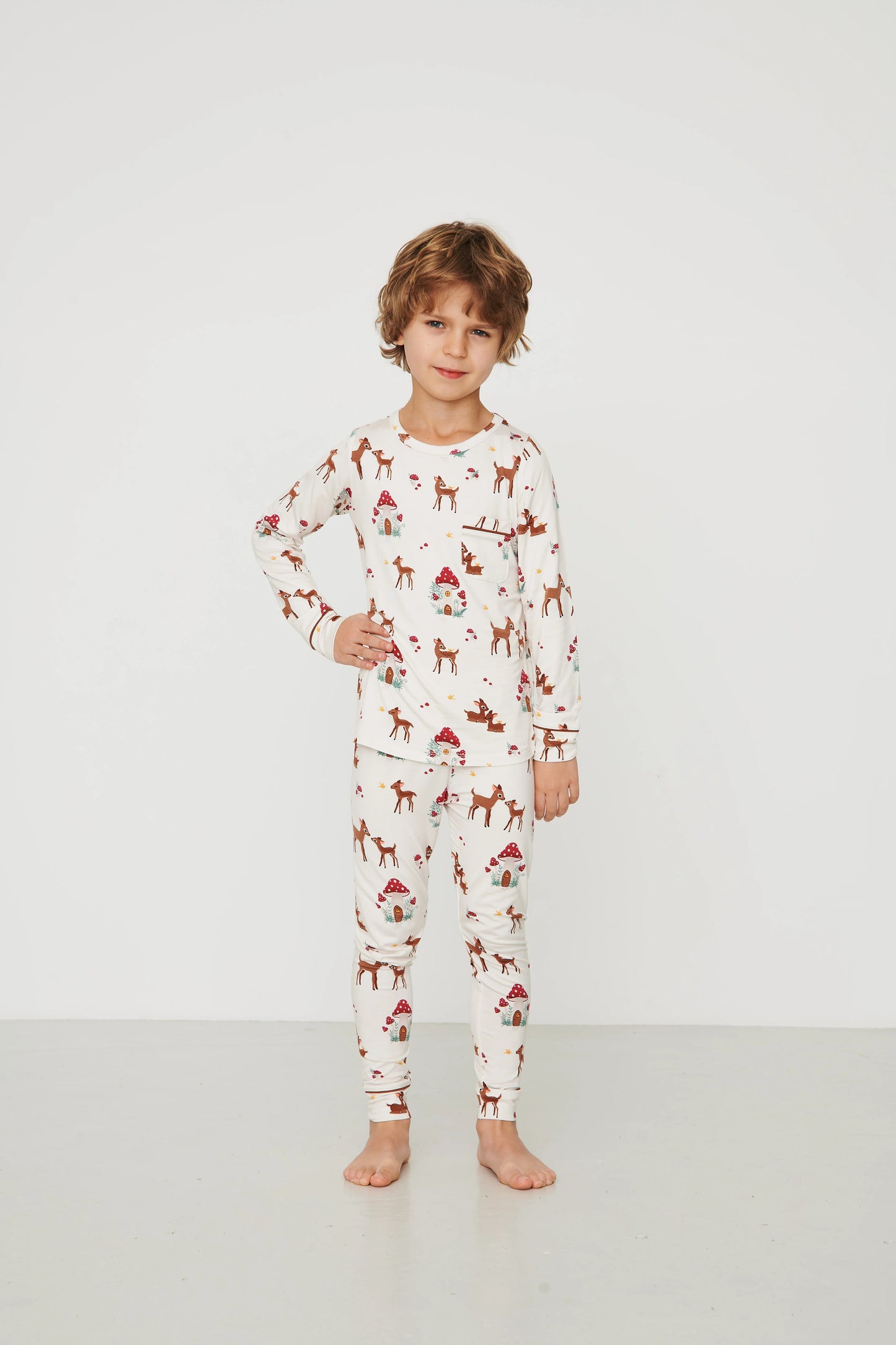 
                  
                    A young child stands barefoot in a studio wearing a long-sleeve pajama set on an off-white background.
                  
                