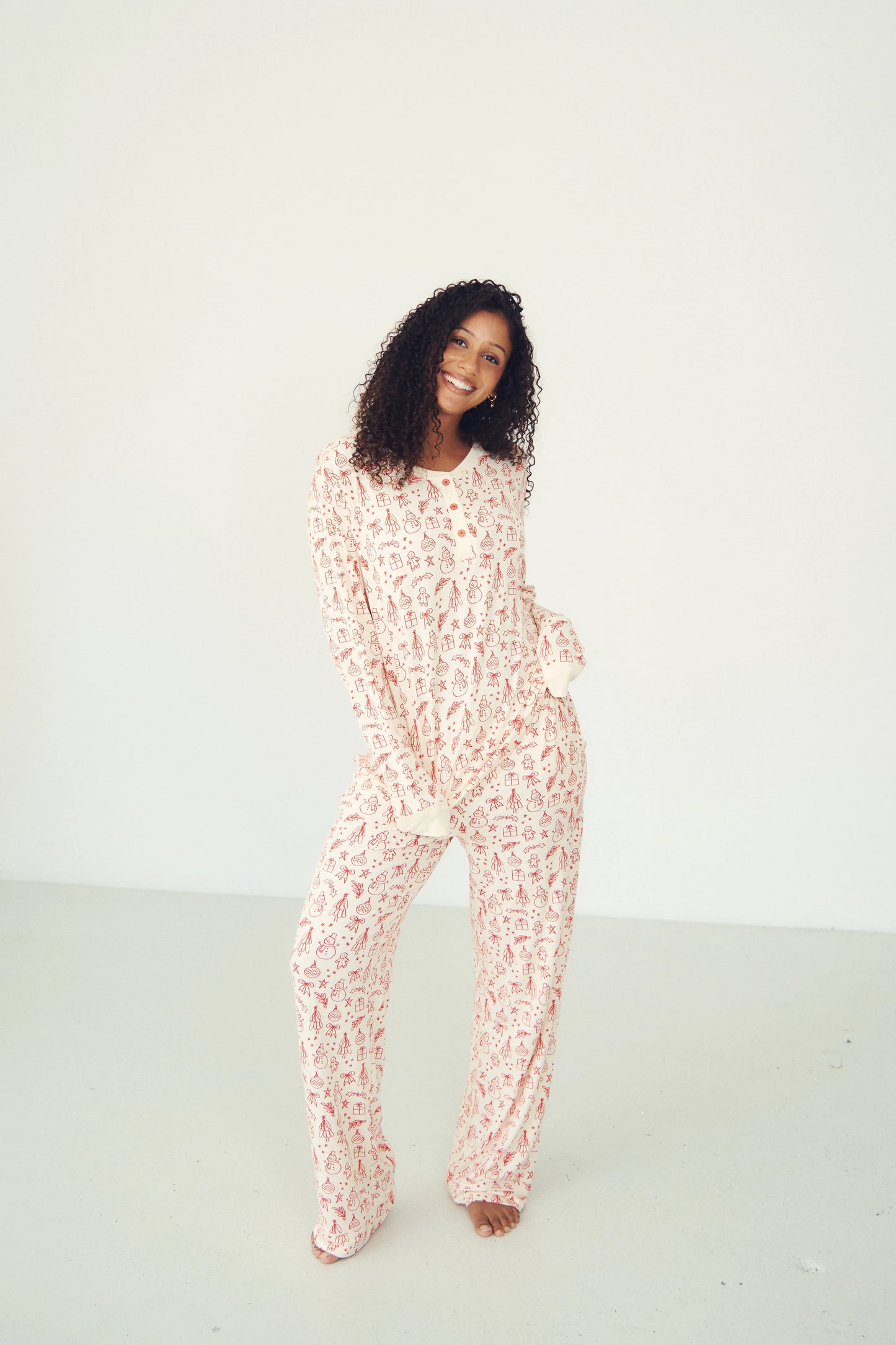
                  
                    A woman modeling a matching long-sleeve pajama set with a red and white Christmas pattern, standing against a plain white studio background.
                  
                