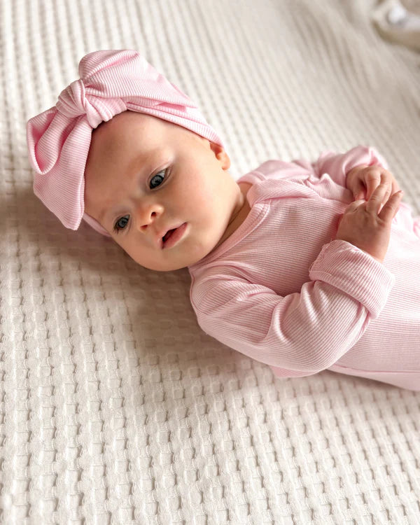 Baby wearing a pink outfit and headband on a textured surface