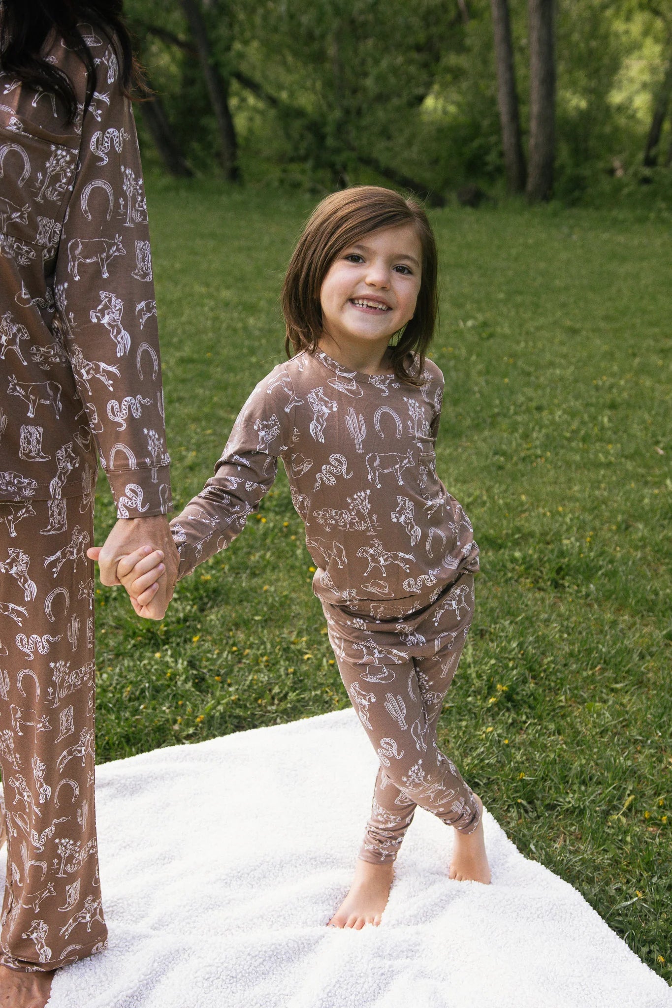 
                  
                    Child wearing a brown pajama set with animal prints on a grassy background.
                  
                
