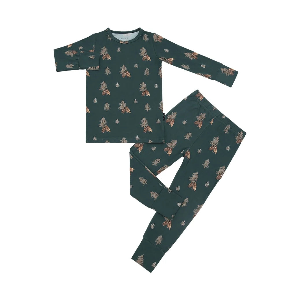 A two-piece children's pajama set featuring a long-sleeve top and matching pants in dark green with an all-over print of pine trees and owls, laid flat on a white background.