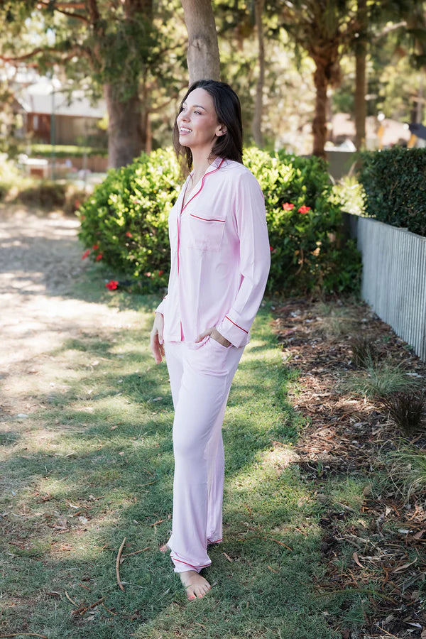 
                  
                    Woman in pink pajamas standing outdoors on a grassy area with trees and plants in the background.
                  
                