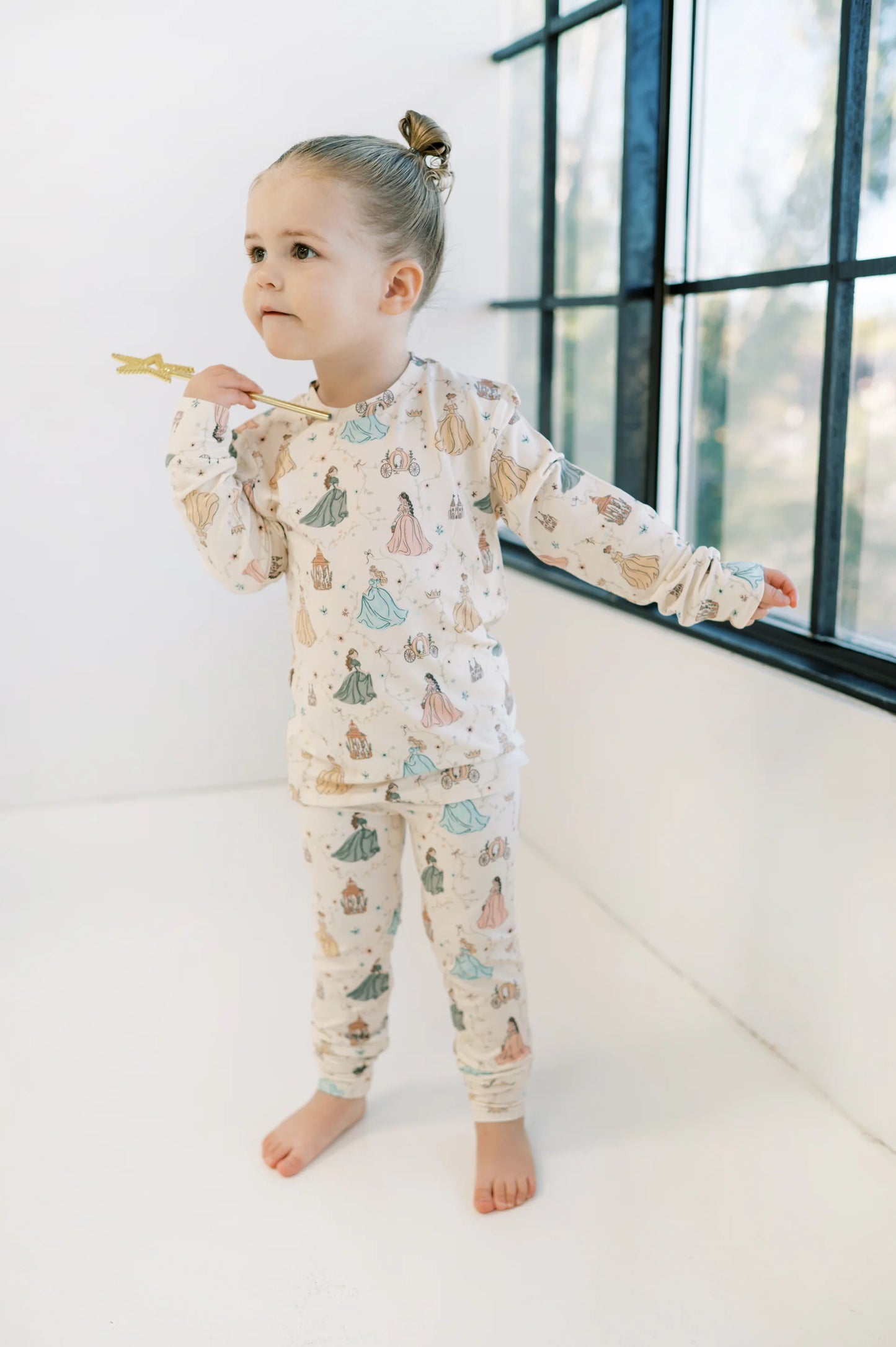 
                  
                    Child in a bamboo lounge set with a princess print standing in front of a window. 
                  
                