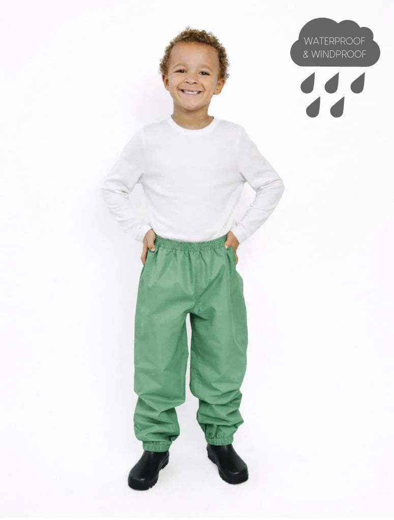 
                  
                    Child wearing green waterproof pants and a white shirt on a white background
                  
                