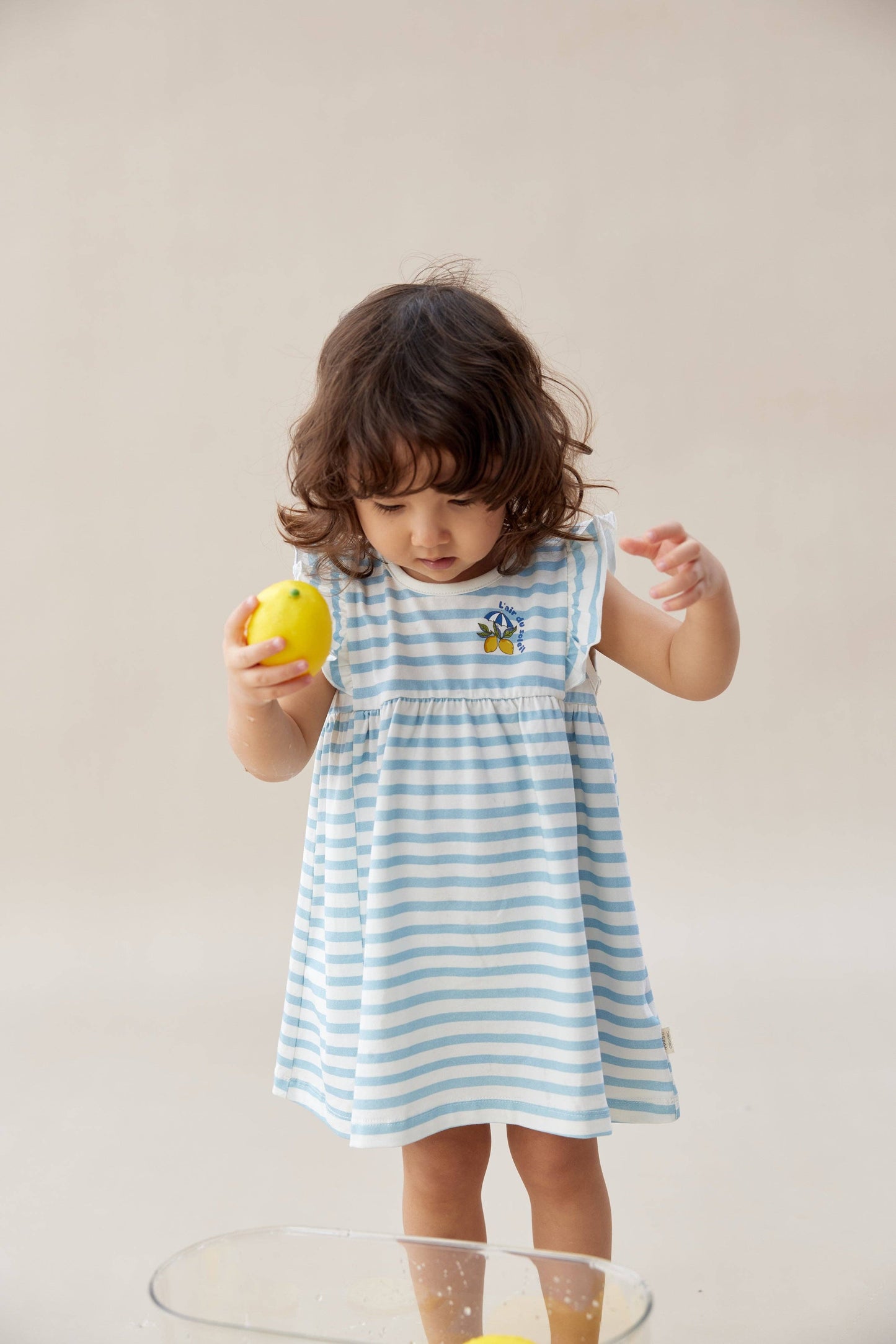 
                  
                    Child wearing a blue and white striped dress holding a lemon.
                  
                
