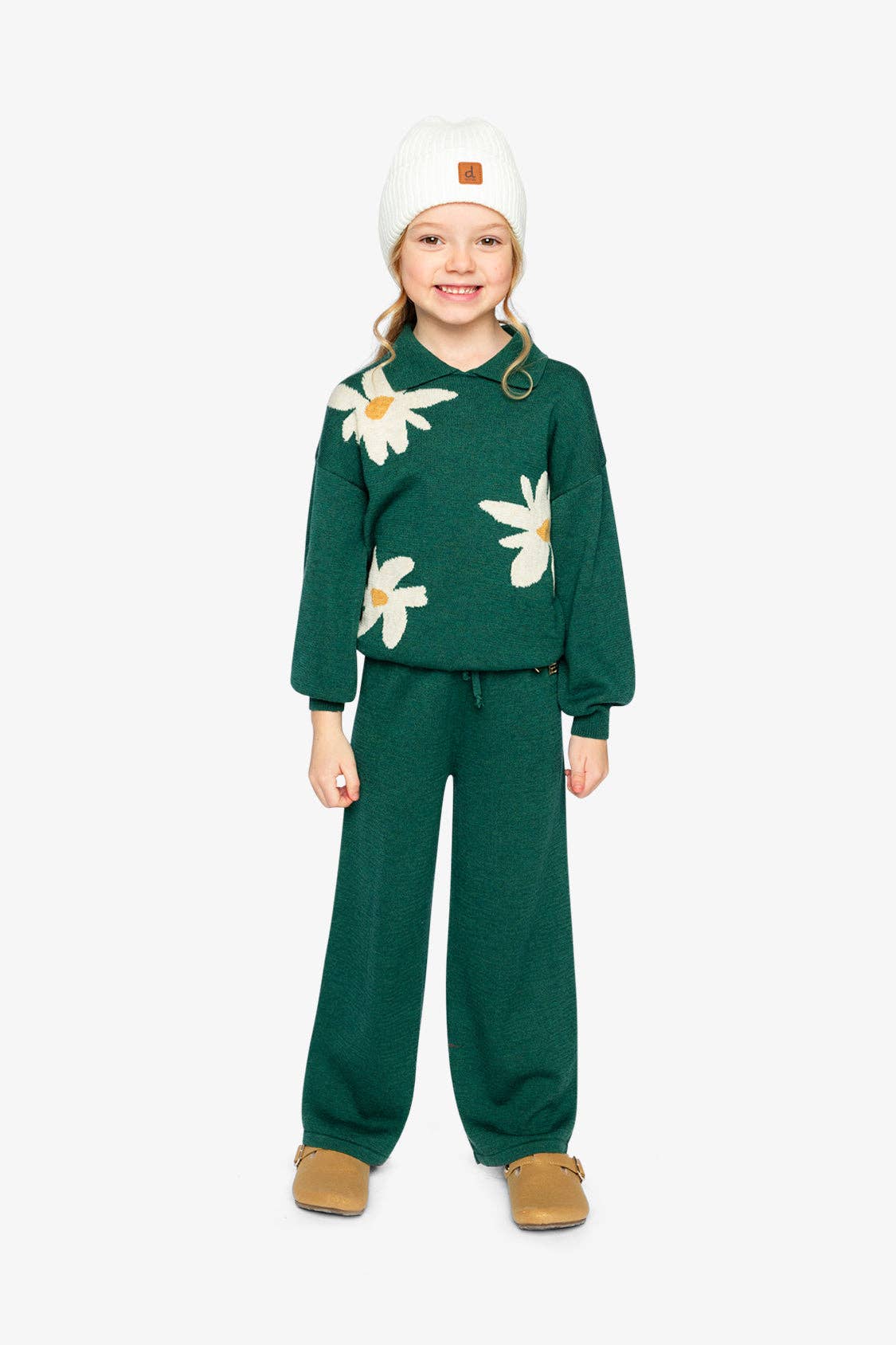 
                  
                    Child wearing a green outfit with floral patterns on a white background.
                  
                