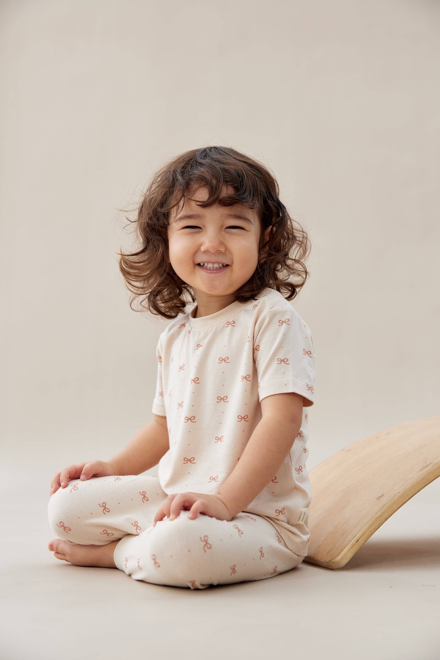 
                  
                    Child wearing a white outfit with small patterns, sitting on a beige surface.
                  
                