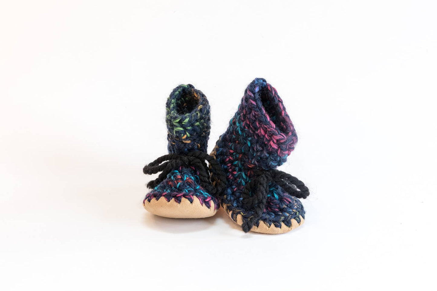 
                  
                    A pair of handmade crocheted booties with black yarn laces and beige soles, shown on a plain white background.
                  
                