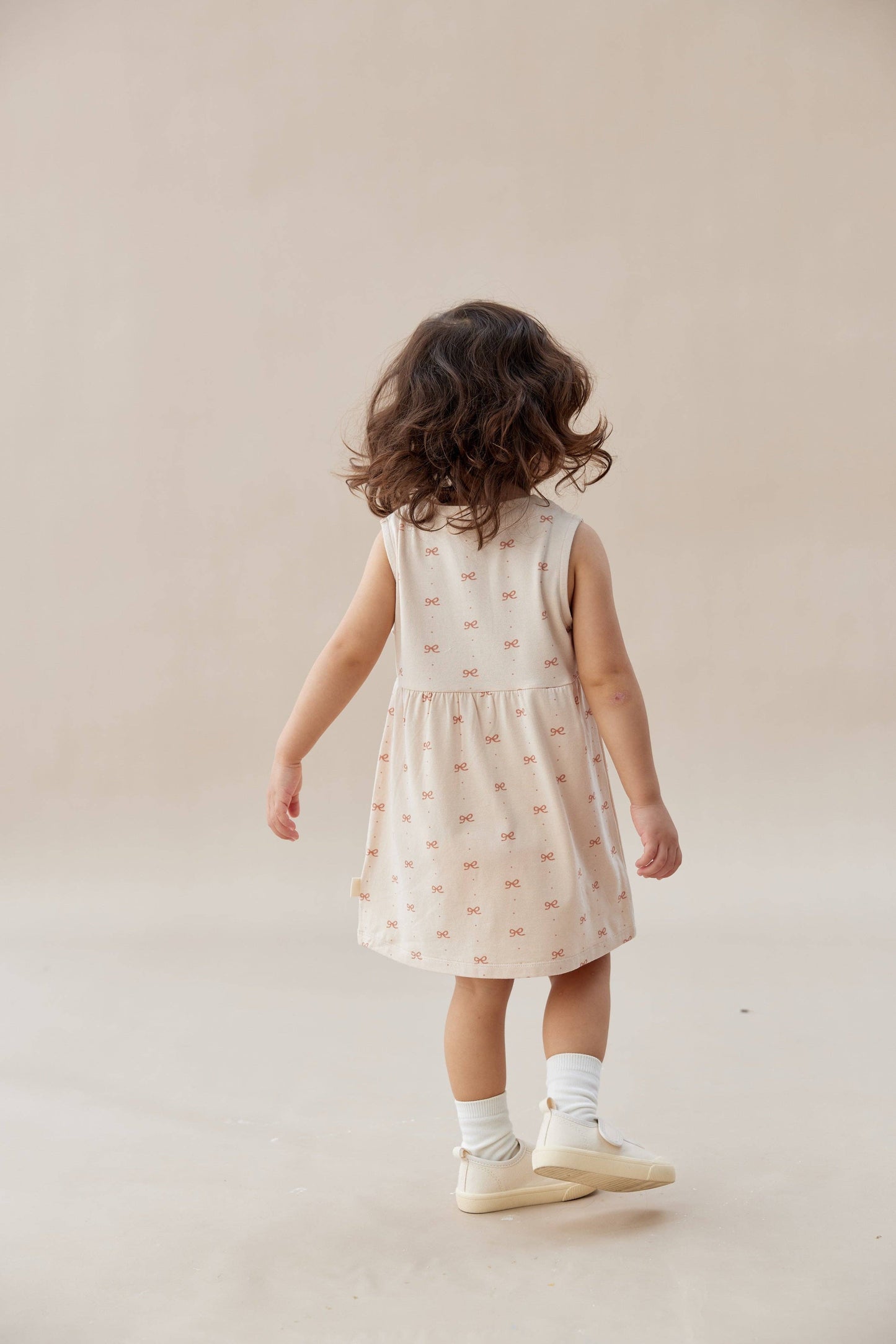 
                  
                    Child wearing a sleeveless dress with a pattern on a plain background.
                  
                