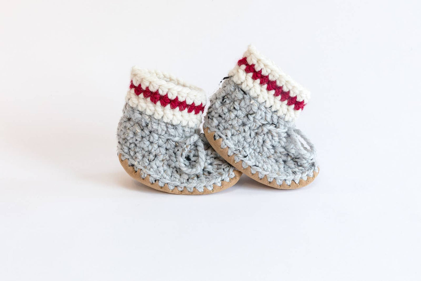 
                  
                    A pair of hand-crocheted baby slippers with a soft sole and wool booties, featuring a red and white pattern.
                  
                
