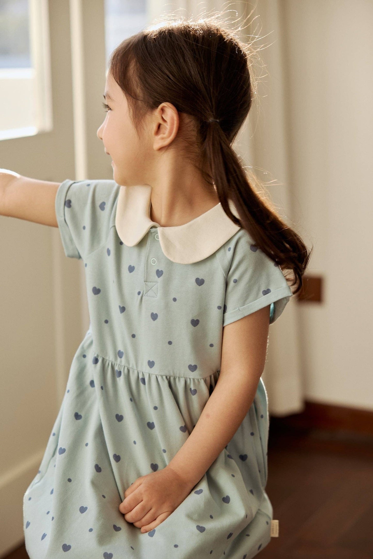 
                  
                    Young girl wearing a light blue dress with heart patterns indoors.
                  
                
