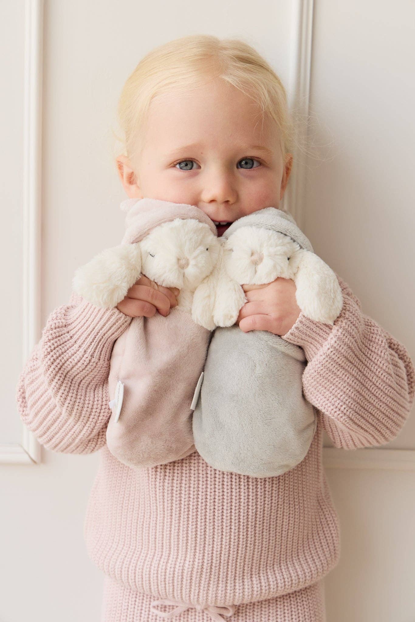 
                  
                    Child holding two plush toys against a white background.
                  
                