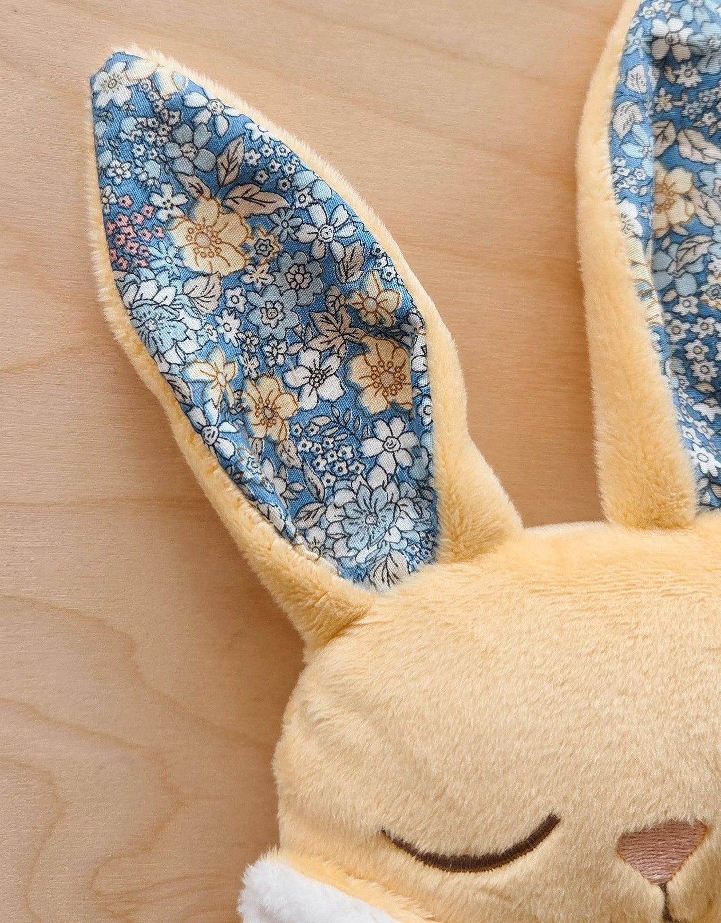 
                  
                    Close-up of a plush toy with floral-patterned ears on a wooden surface.
                  
                