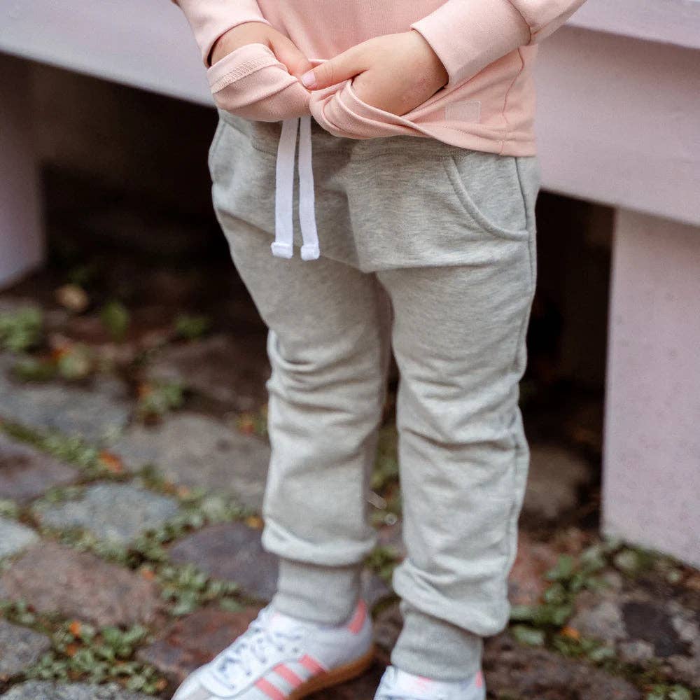 
                  
                    Child wearing light gray sweatpants and pink hoodie on a stone path.
                  
                