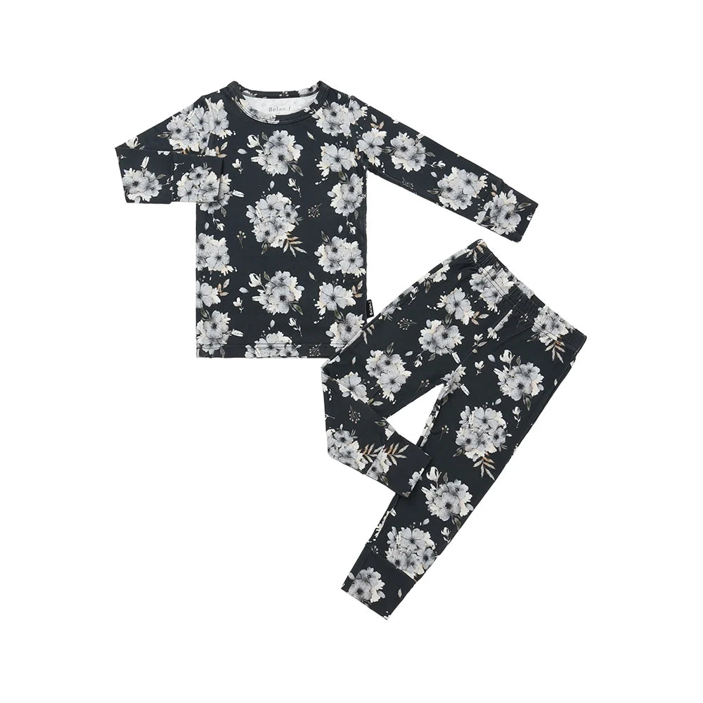 A two-piece children's pajama set featuring a long-sleeve top and matching pants in a dark navy blue floral print with white and light gray flowers and small yellow accents, laid flat on a white background.