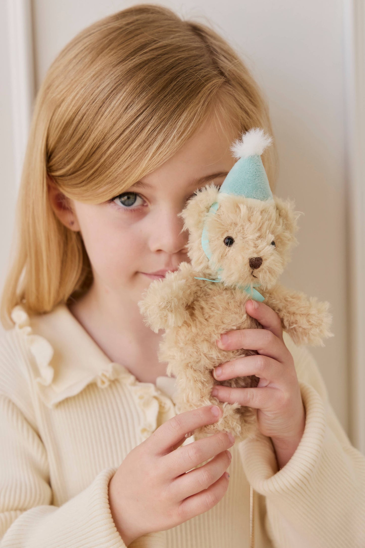 
                  
                    Child holding a teddy bear with a party hat indoors.
                  
                