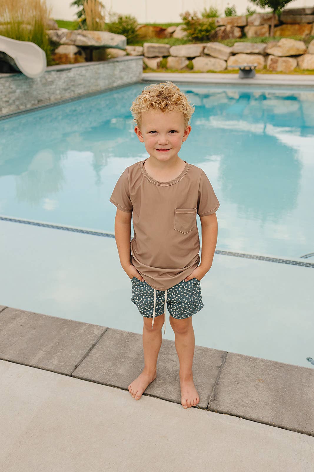 
                  
                    Child standing by a pool with a scenic background
                  
                
