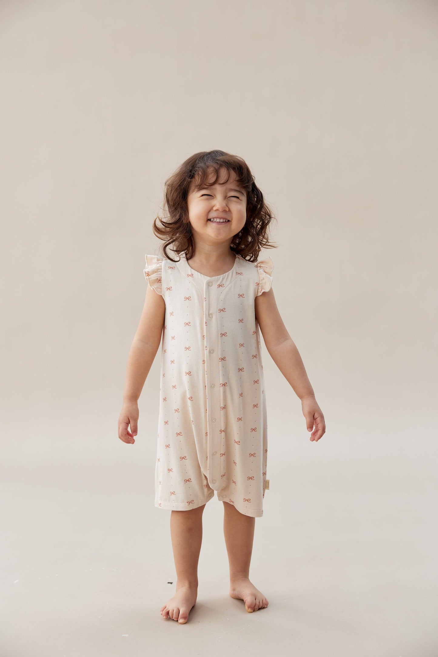 Child wearing a light-colored romper with a subtle pattern on a plain background.