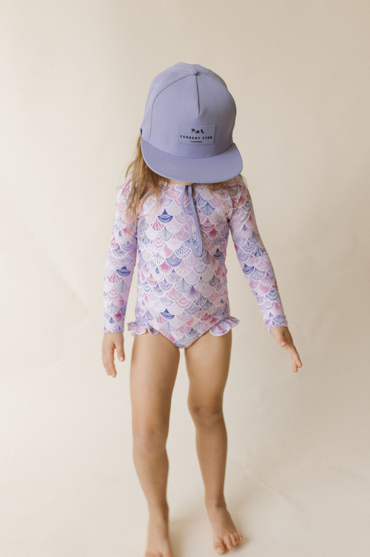 
                  
                    Child wearing a colorful swimsuit and purple cap on a beige background
                  
                