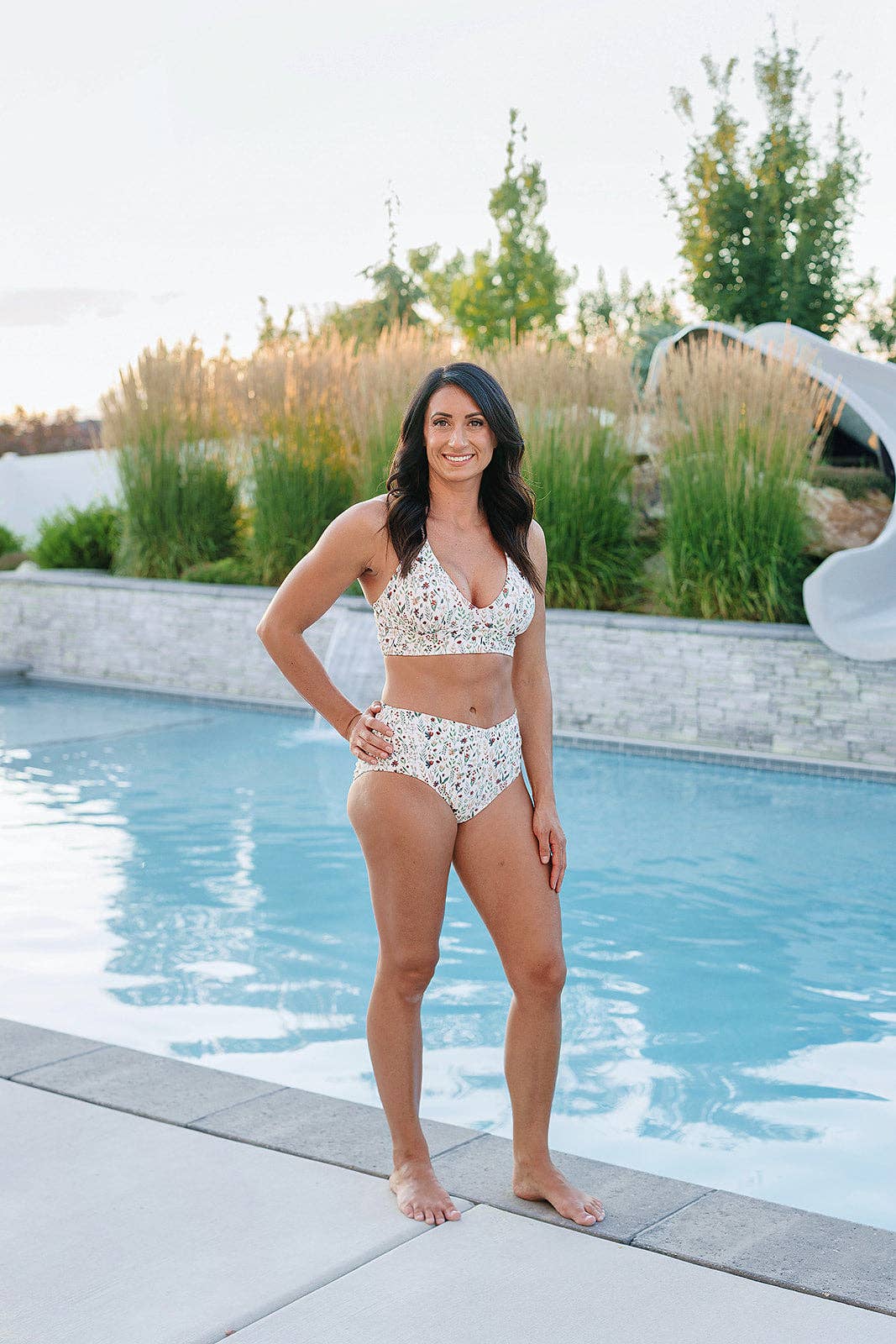 Woman in a floral bikini standing by a pool with greenery in the background