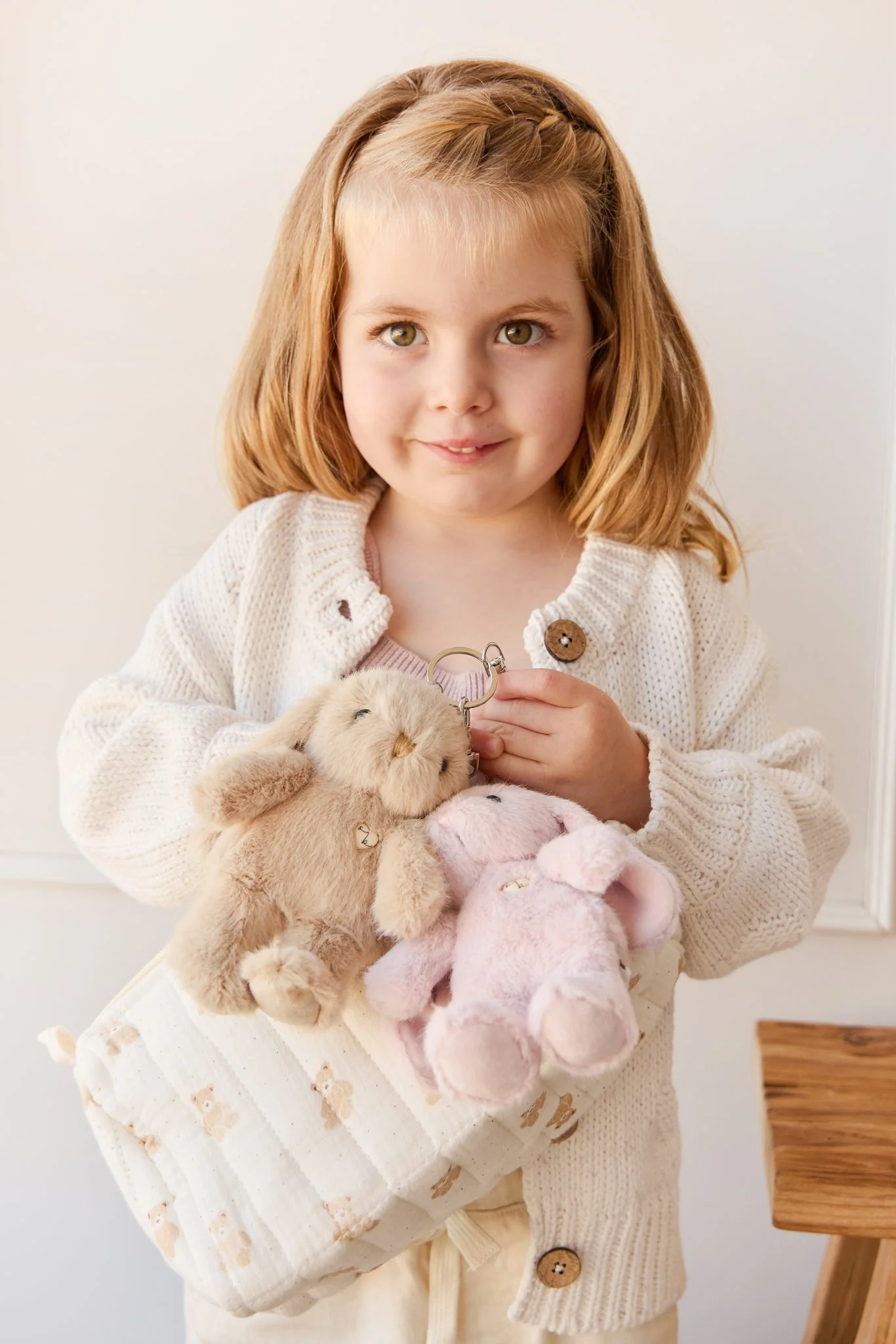 
                  
                    Young girl holding a bag with plush bunny keychains indoors.
                  
                