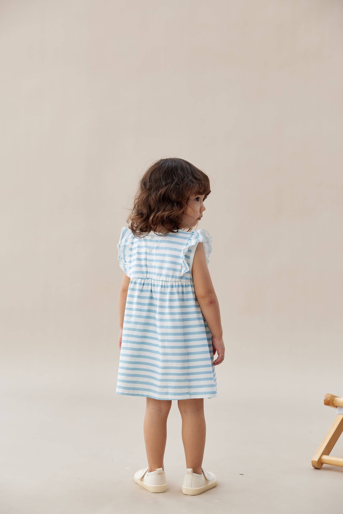 
                  
                    Young girl wearing a blue and white striped dress against a plain background.
                  
                
