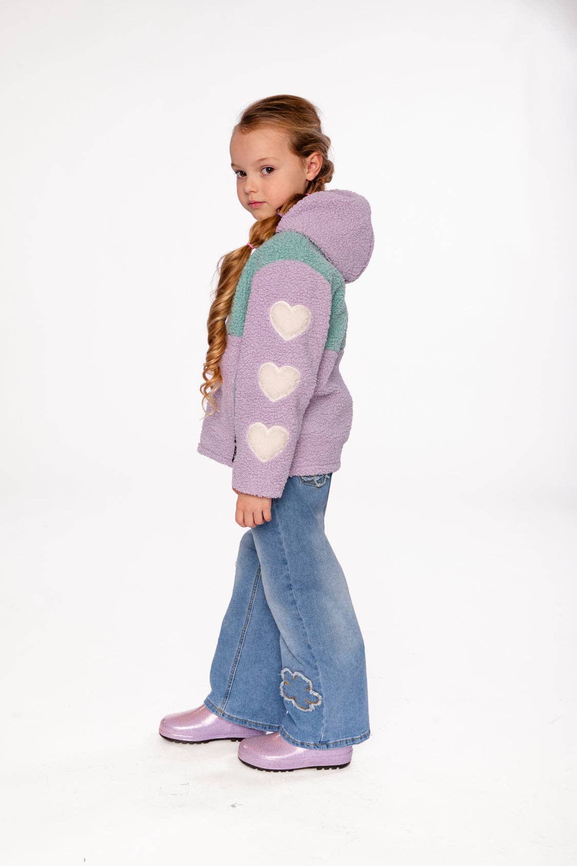 
                  
                    Young girl wearing a purple hoodie with heart patterns and blue jeans on a white background.
                  
                