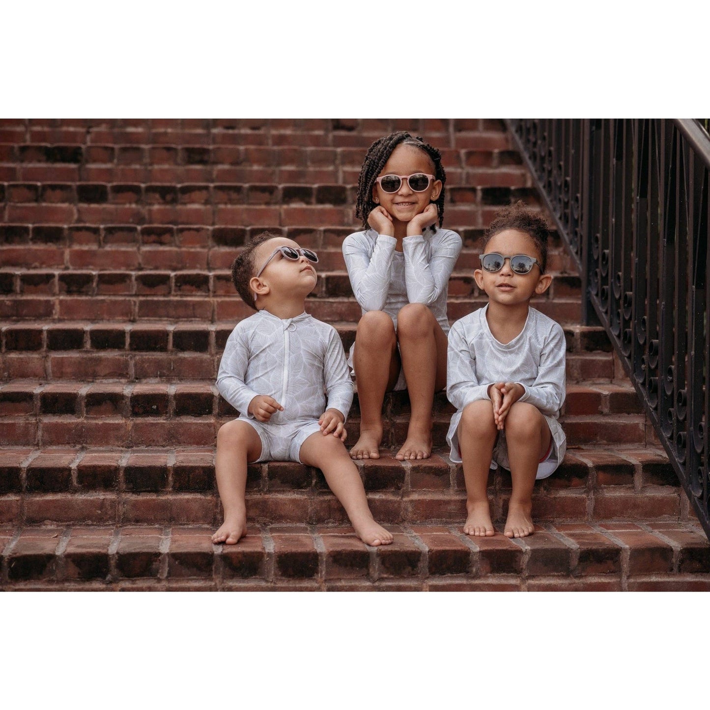 Three children sitting on a brick staircase wearing sunglasses.