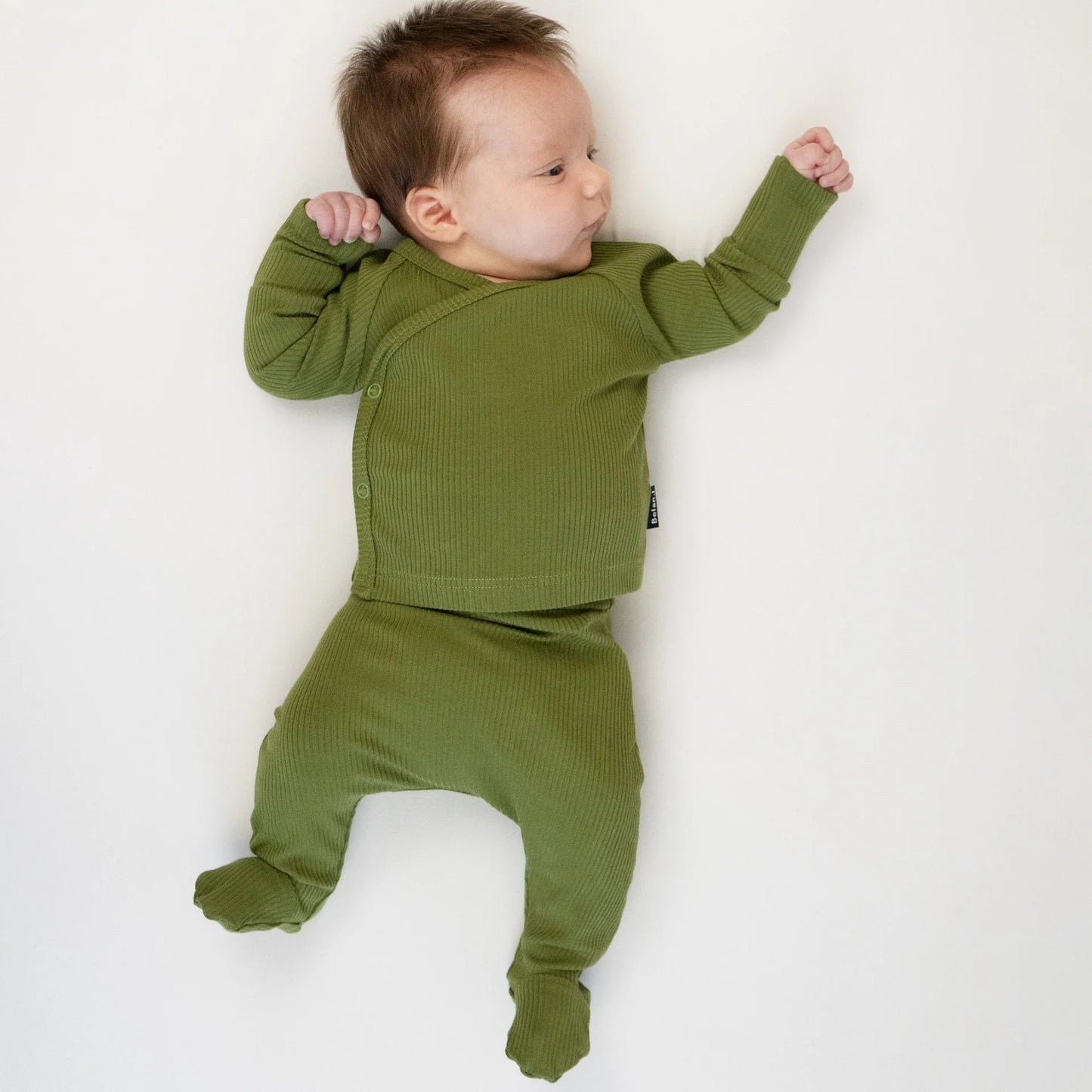
                  
                    A baby lying on their back wearing an olive green ribbed long-sleeve footed sleeper against a plain white background.
                  
                