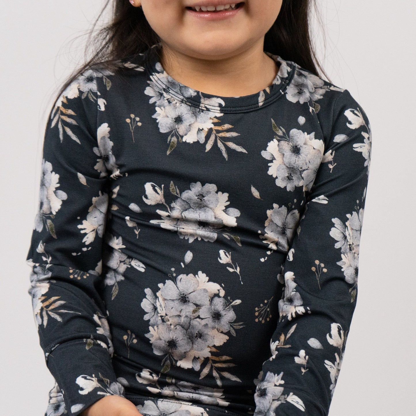 
                  
                    A close-up of a child wearing a long-sleeve crewneck shirt with a dark navy blue base and a light gray and white floral pattern.
                  
                