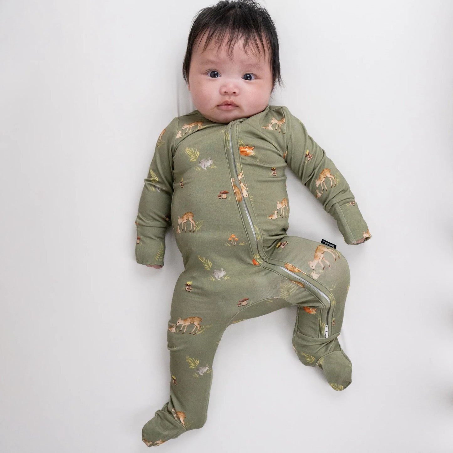
                  
                    A baby wearing an olive green footed sleeper with a small woodland animal print, lying on a light gray background.
                  
                